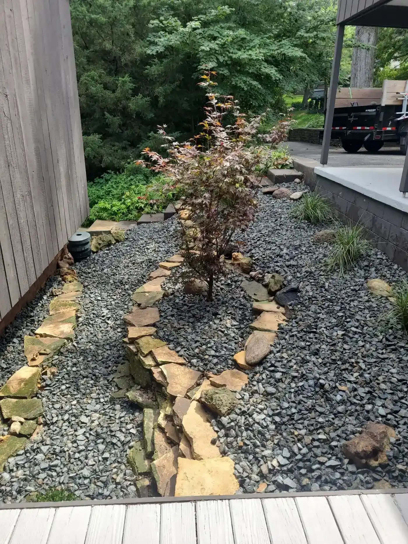 Dry creek bed of river rock and stone edging with a small tree along a side yard