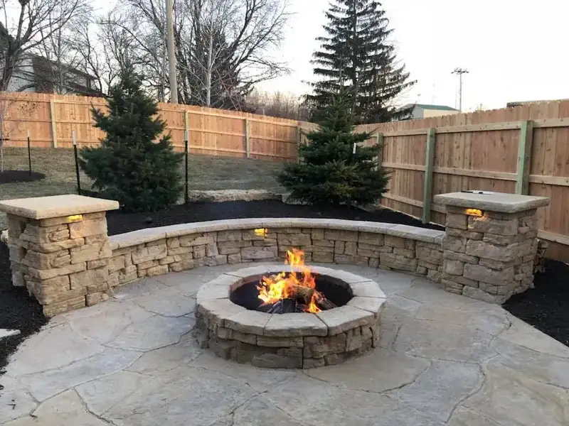 Stone fire pit burning inside a curved seat wall with lighted pillars