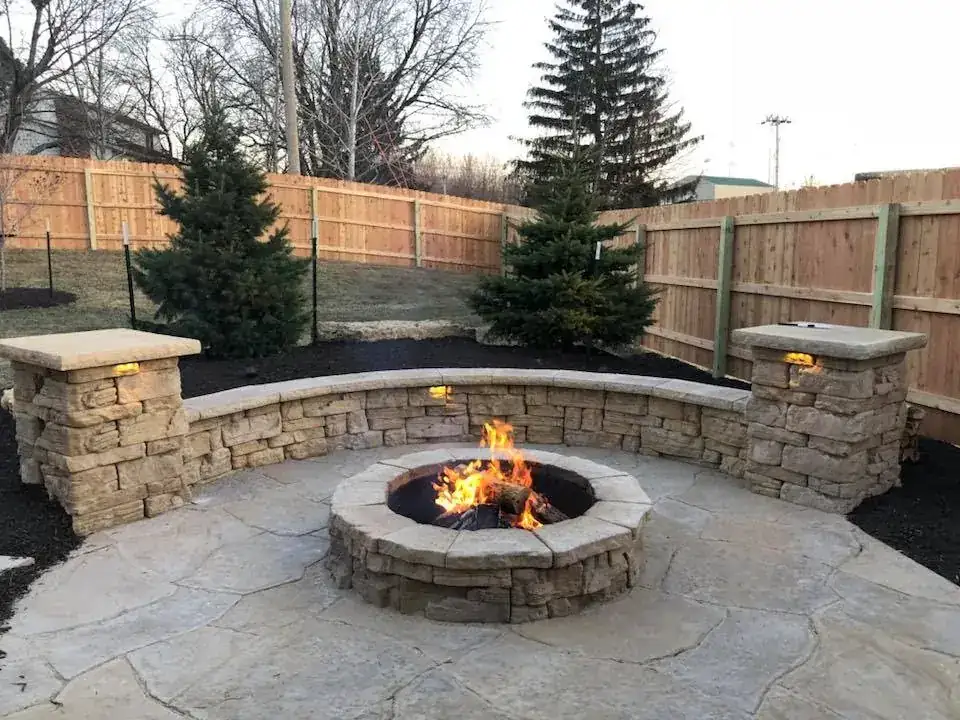Curved stone seat wall with pillar caps around a burning fire pit