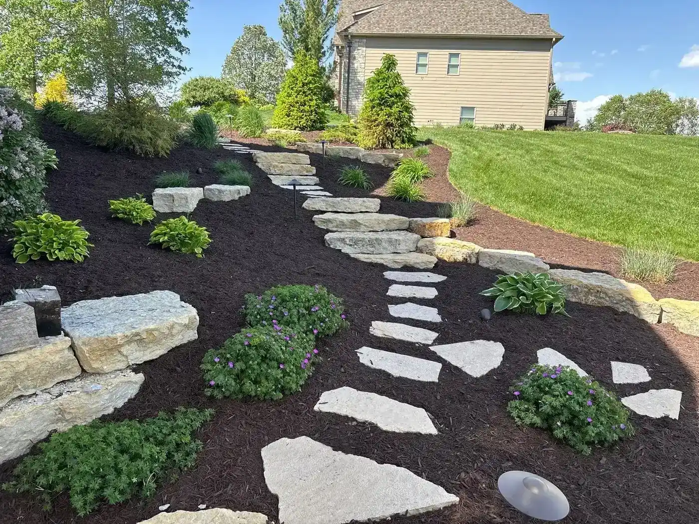 Flagstone stepping-stone path winding through fresh mulch beds with new shrubs and boulders