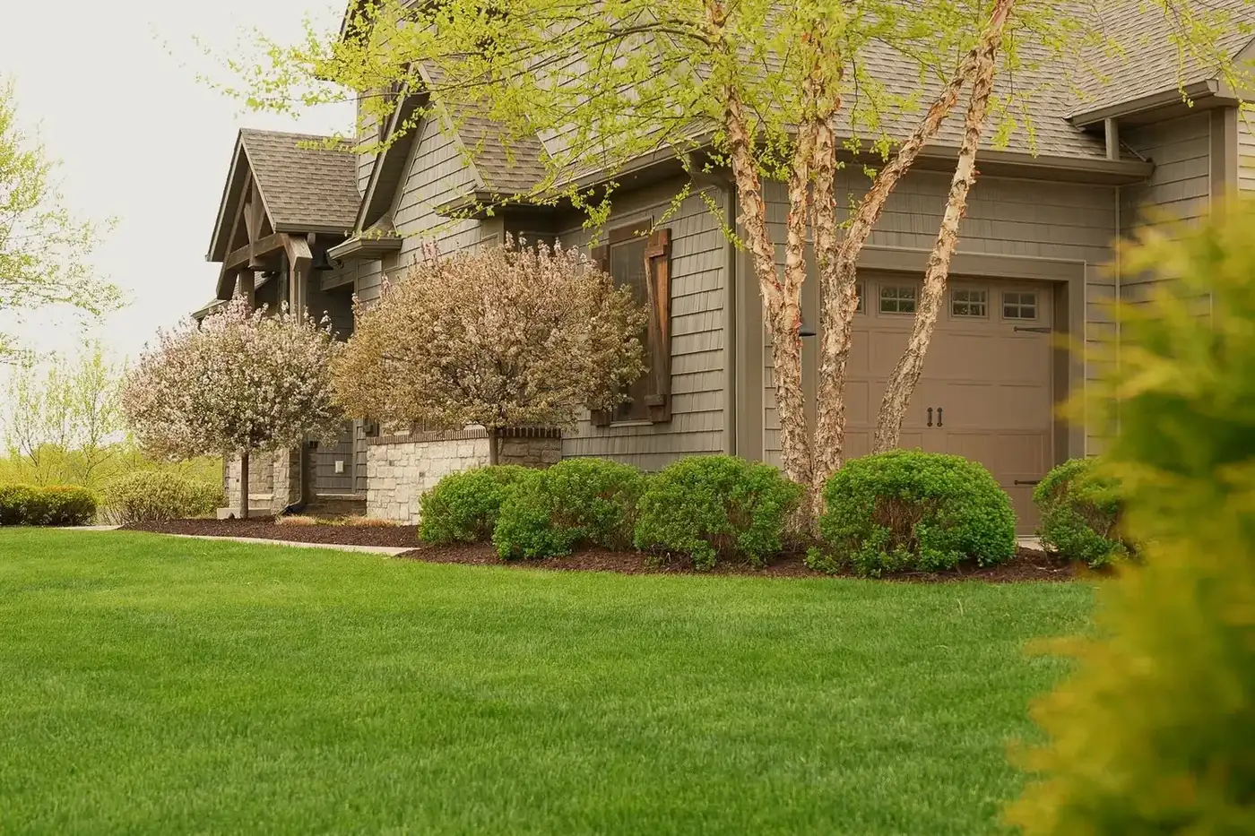 Trimmed shrubs and clean mulch beds in front of a home with a green lawn