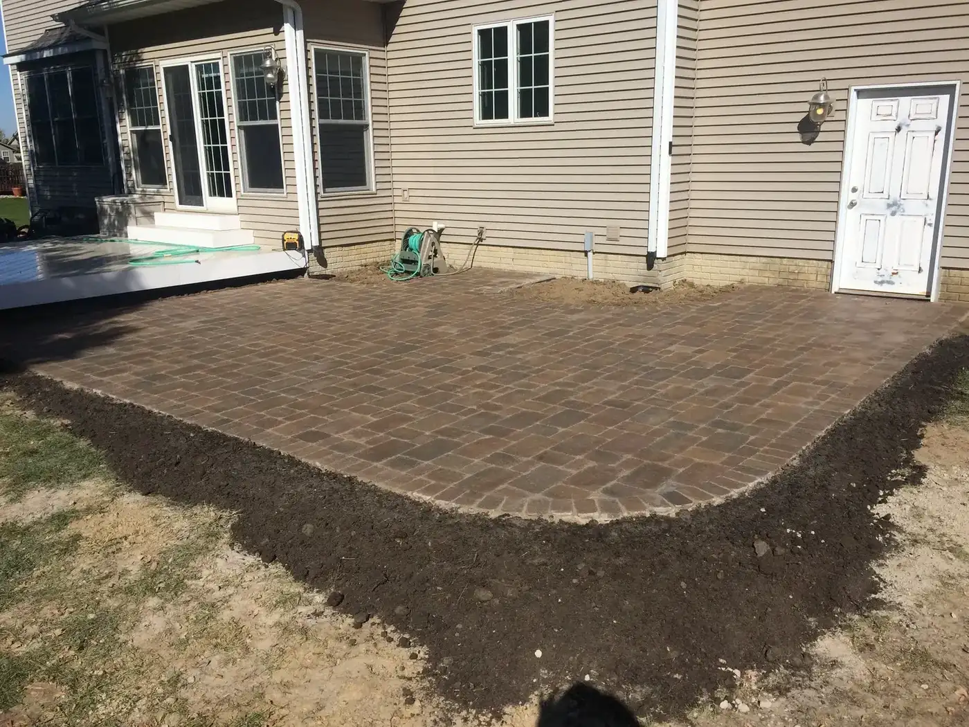 Finished paver patio behind a tan two-story house