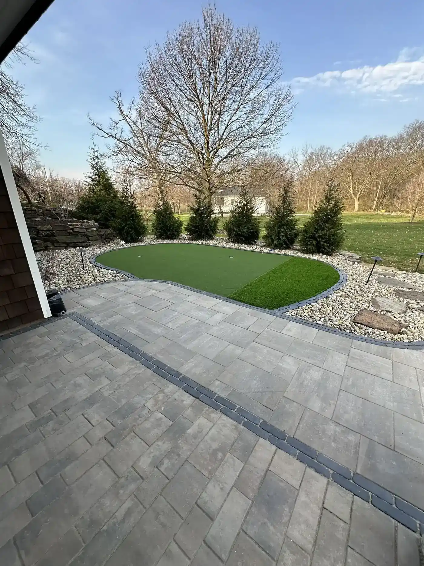 Paver walkway beside a small artificial turf area and rock beds