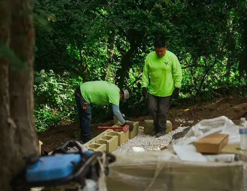 Crew setting block on a retaining wall under trees