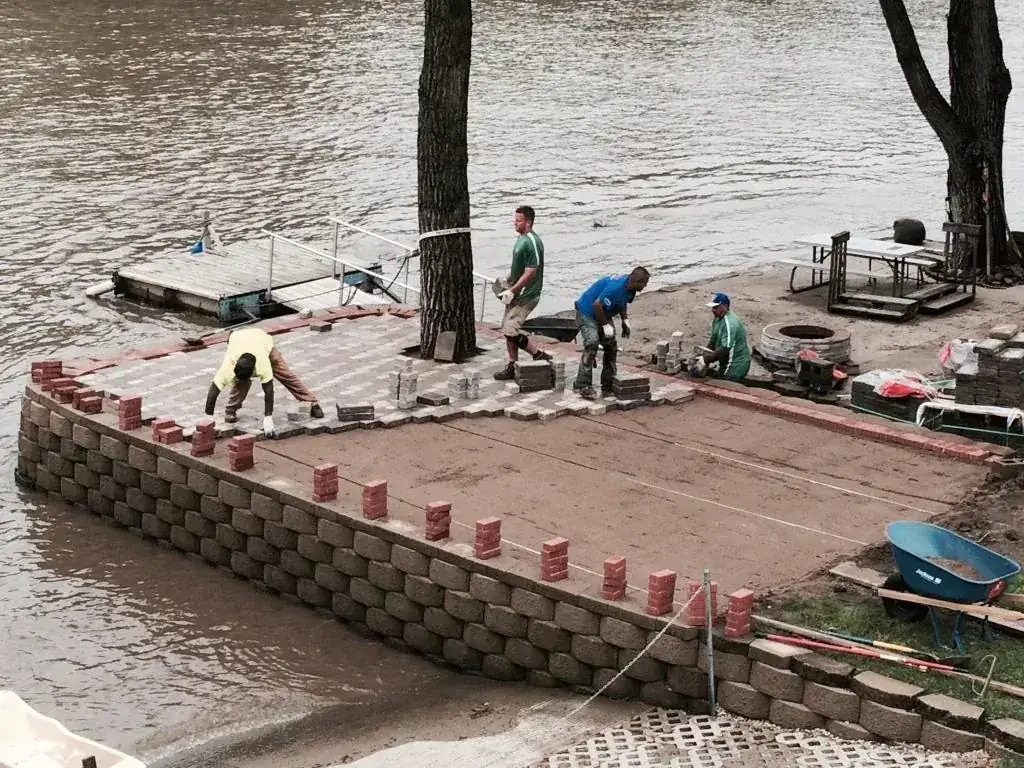 Crew building a paver patio at the edge of a river
